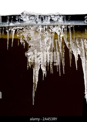 Eiszapfen und Schnee auf dem Dach Nahaufnahme. Winter Wetter Konzept. Erstarrte und Eis Hintergrund. Schnee und Eiszapfen. Schmelzenden Eiszapfen. Eiszapfen und Schnee auf dem Dach closeup Stockfoto