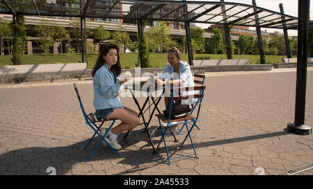 Mutter und Tochter im Cafe Tabelle mit blauen Jacken und Park im Hintergrund sitzen Stockfoto