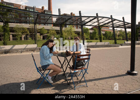 Mutter und Tochter im Cafe Tabelle mit blauen Jacken und Park im Hintergrund sitzen Stockfoto