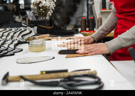 Schuster ist das Hinzufügen von Klebstoff mit einem Pinsel einige Stücke aus Leder, die verwendet werden, um Schuhe zu machen. Der Schuster arbeitet an seinem Schreibtisch in seinem Workshop Stockfoto