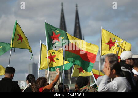 Köln, Deutschland. 12 Okt, 2019. Die Teilnehmer halten Fahnen während der Demonstration top Die Invasion der kurdischen Gebiete" an der Deutzer Werft mit dem Kölner Dom im Hintergrund. 5000 Teilnehmer sind für die Rallye angemeldet. Quelle: David Young/dpa/Alamy leben Nachrichten Stockfoto