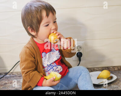 Kleines Kind isst eine Birne. Kind junge Früchte essen auf einem hohen stoisch. in der Küche. Stockfoto