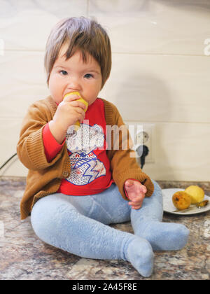 Kleines Kind isst eine Birne. Kind junge Früchte essen auf einem hohen stoisch. in der Küche. Stockfoto