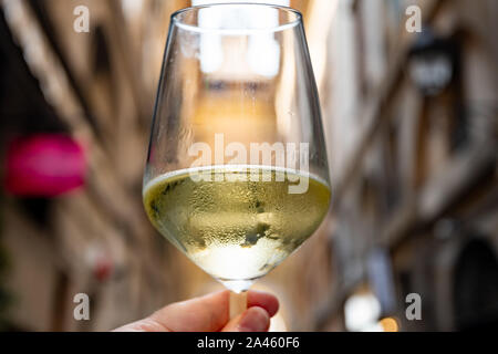 Hand hält ein Weißweinglas, um mit Stadtgebäuden im Hintergrund zu toasten. Stockfoto