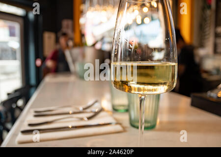 Aufnahme eines Restaurantthekens mit einem Glas Weißwein aus der Nähe und einem unfokussten Blick auf eine moderne Location im Hintergrund. Stockfoto