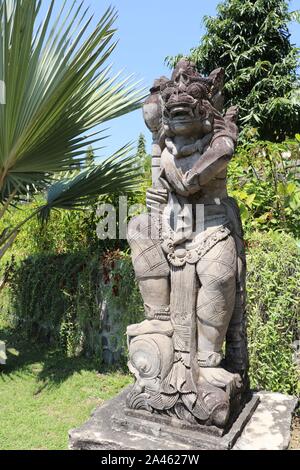 Statue aus weißem Stein in tropischen Garten zwischen den Blumen auf der Insel Bali. Eine Darstellung der Beschützer der balinesischen hinduistischen Mythologie. Sonnigen Tag. Stockfoto