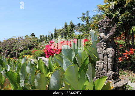 Statue aus weißem Stein in tropischen Garten zwischen den Blumen auf der Insel Bali. Eine Darstellung der Beschützer der balinesischen hinduistischen Mythologie. Sonnigen Tag. Stockfoto