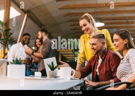 Junge Kolleginnen und Kollegen arbeiten am Laptop und diskutieren neue Projekt Stockfoto