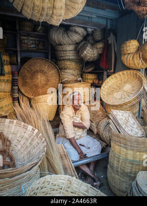 MYSURU (MYSORE), Karnataka/Indien - 15 Februar 2018: Am Devaraja Market ein geflochtener Korb Verkäufer spricht mit einer Frau als sitzt er durch seine Waren umgeben. Stockfoto