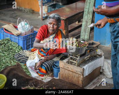 MYSURU (MYSORE), Karnataka/Indien - vom 15. Februar 2018: Devaraja Market, einer älteren weiblichen pflanzliche Verkäufer wiegt Sie produzieren auf den traditionellen Maßstäben für ein Cust Stockfoto