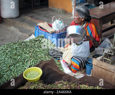 MYSURU (MYSORE), Karnataka/Indien - vom 15. Februar 2018: Devaraja Market, einer älteren weiblichen pflanzliche Verkäufer wiegt Sie produzieren auf den traditionellen Maßstäben für ein Cust Stockfoto