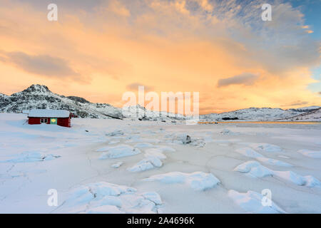 Lofoten in Norwegen und ihre schönen Winterlandschaft bei Sonnenuntergang. Idyllische Landschaft mit roten Haus auf Schneebedeckter Strand. Touristenattraktion in Stockfoto