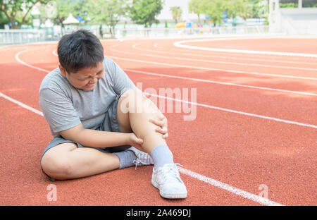 Asiatische Fat Boy, seinen Sport Beinverletzung Holding. Muskel schmerzhaft beim Training. kid Runner in Kalb Ache und das Problem nach dem Ausführen auf Schiene. sport und Stockfoto