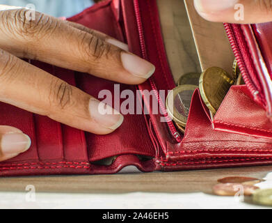 Nahaufnahme der schwarzen Frau Hände ihre rote Geldbörse öffnen Mit wenigen Euro Münzen innen. Seletive Fokus auf der Handtasche. Stockfoto