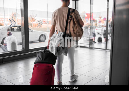 Rückansicht des zuversichtlich, dass man in lockerer Kleidung entlang Lounge im Flughafen, während sein Gepäck tragen Stockfoto