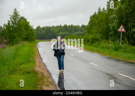 Eine alte Frau geht auf einer nassen Straße, im Wald ist. Stockfoto