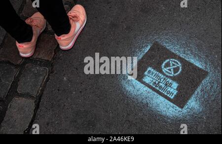 12. Oktober 2019, Berlin: eine Umweltaktivistin aus Aussterben Rebellion steht auf der Stresemannstraße neben dem Logo der Allianz auf die Straße gesprüht. Umweltaktivisten von Aussterben Rebellion blockieren Sie die stresemannstraße vor dem Bundesumweltministerium. Nach der ökologischen Bewegung Aussterben Rebellion (XR), mehrere hundert Aktivisten versammelten sich am Samstag Nachmittag vor dem Bundesministerium für Umwelt, Naturschutz und Reaktorsicherheit und andere Teile der Stresemannstraße in der Nähe von Potsdamer Platz. Die stresemannstraße bis Sonntag besetzt werden, sagten sie. Foto: Paul Zinken/dpa Stockfoto