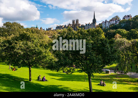 Die Princes Street, Edinburgh, Schottland, Großbritannien, 12. Oktober 2019. UK Wetter: Menschen in Edinburgh einen schönen warmen sonnigen Herbsttag in der Hauptstadt genießen. Die Leute sitzen auf dem Rasen mit Blick auf Ramsey Gärten Stockfoto