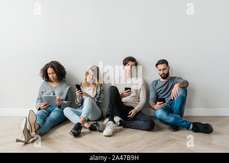 Interkulturelle milennials mit Smartphones durch weiße Wand saß während texting Stockfoto