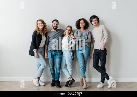 Happy interkulturelle Jungs und Mädchen in der casualwear stehend gegen weiße Wand Stockfoto