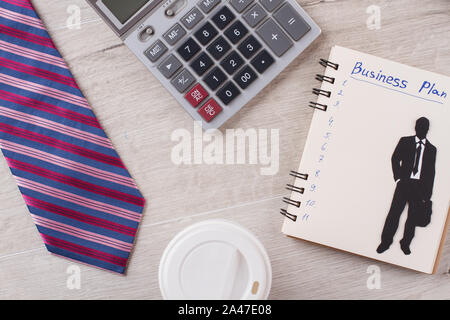 Krawatte, Taschenrechner und Kaffeebecher im Fokus. Stockfoto