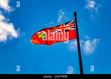 Die Flagge der kanadischen Provinz Ontario fliegt im Wind vor blauem Himmel. Er bläst, links neben dem Fahnenmast vor einem strahlend blauen Himmel. Stockfoto