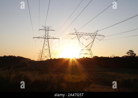 Die Sonne hinter ein paar hoch aufragenden Strommasten Stockfoto