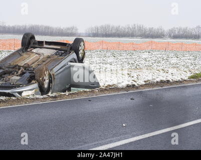 Umgeworfen Auto neben der nassen Straße an einem Wintertag Stockfoto