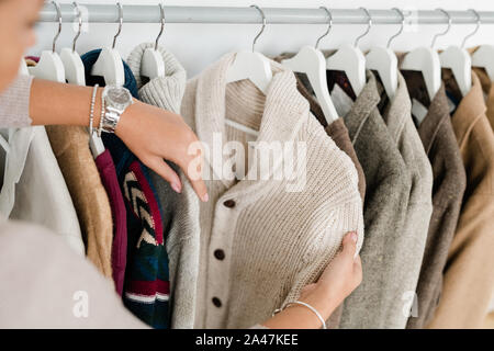 Die Hände der jungen Frau mit weißen Strickjacke, während Sie neue Kleider Stockfoto