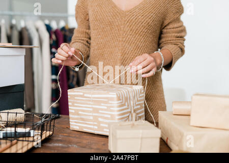 Junge Frau in casual Strickpullover verbindliche Gewinde an verpackte Geschenkset Stockfoto