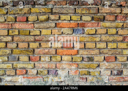 Oberfläche des gealterten rauhe Wand Rot Gelb und Grau gebrochene Steine mit Zementmörtel. Abstrakte vintage Hintergrund. Hintergrund für die Textur. Stockfoto