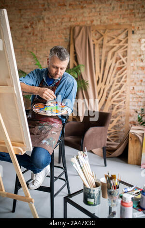 Zeitgenössische Maler in casualwear und Schürze Mischen von Farben auf der Palette Stockfoto