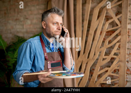 Gereizt oder verwirrt im mittleren Alter Maler mit Handy und Palette Stockfoto