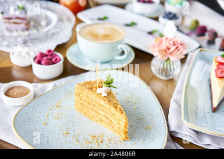 Honig Kuchen mit Baiser und Minze dekoriert.. Frühstück im Café, Kaffee am Morgen. Cappuccino und viele Desserts auf dem Tisch. Stockfoto