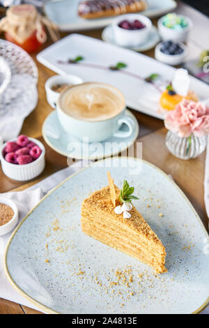 Honig Kuchen mit Baiser und Minze dekoriert.. Frühstück im Café, Kaffee am Morgen. Cappuccino und viele Desserts auf dem Tisch. Stockfoto