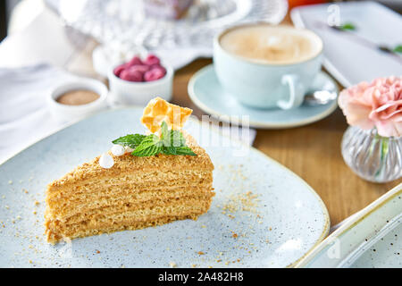 Honig Kuchen mit Baiser und Minze dekoriert.. Frühstück im Café, Kaffee am Morgen. Cappuccino und viele Desserts auf dem Tisch. Stockfoto