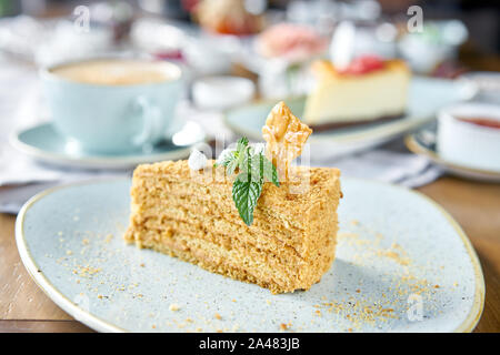 Honig Kuchen mit Baiser und Minze dekoriert.. Frühstück im Café, Kaffee am Morgen. Cappuccino und viele Desserts auf dem Tisch. Stockfoto