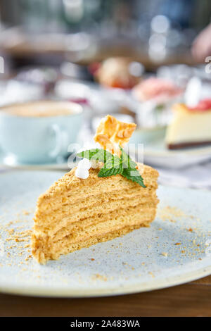 Honig Kuchen mit Baiser und Minze dekoriert.. Frühstück im Café, Kaffee am Morgen. Cappuccino und viele Desserts auf dem Tisch. Stockfoto