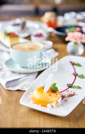 Gelbe mousse-Kuchen. Frühstück im Café, Kaffee am Morgen. Cappuccino und viele Desserts auf dem Tisch. Französische Dessert, Blaubeere, Minze und ein Stück Stockfoto