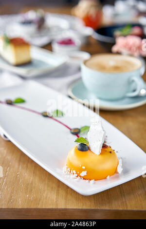 Gelbe mousse-Kuchen. Frühstück im Café, Kaffee am Morgen. Cappuccino und viele Desserts auf dem Tisch. Französische Dessert, Blaubeere, Minze und ein Stück Stockfoto