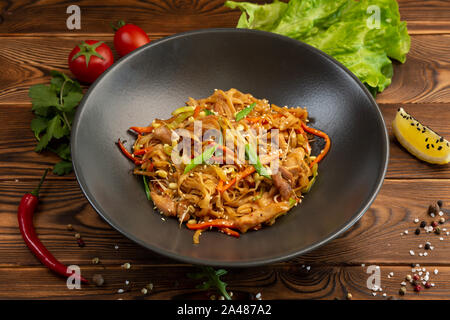 Tori udon Weizen gebratene Nudeln mit Huhn und Gemüse und Sojasauce in eine schwarze Platte auf einem hölzernen Hintergrund Stockfoto