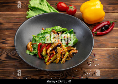 Gebratene Wok Gemüse: Auberginen, Möhren, Champignons, Zucchini, rote Zwiebeln, Soja Sprossen und Spinatblätter in teriyaki Sauce in eine schwarze Platte gebraten auf einem Stockfoto