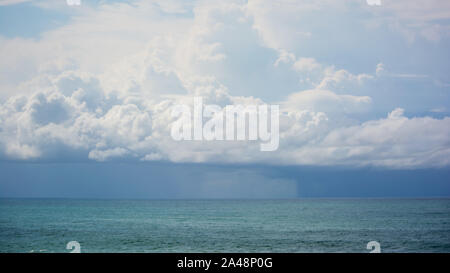 Viele Blautöne in dieser Szene, blaugrünes Meerwasser vor dem niedrigen Cumulonimbus Gewitterwolken am Himmel über dem Ozean, regnet die Ferne, Horizont Stockfoto