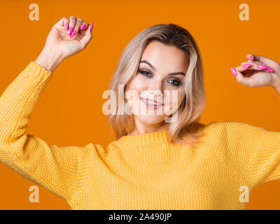 Glücklich und freundlich Blondine in einem gelben Pullover auf gelbem Hintergrund. Positive junge Frau freut und Tänze, Hochformat close-up Stockfoto