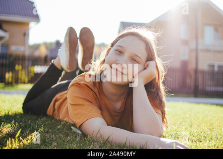 Portrait von lächelnden jugendlich Mädchen liegt auf sonnigen, grünen Gras der Cottage Village auf dem Hintergrund Stockfoto