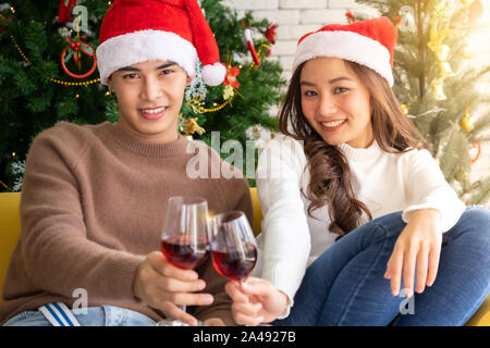 Jungen asiatischen Erwachsene Teenager Paar celebrateing weihnachten urlaub mit Wein zusammen im Wohnzimmer mit Christbaumschmuck. Stockfoto