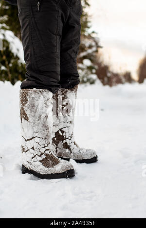 Füße im warmen, komfortablen fühlte Schuhe mit Schnee zu Ihnen nach einem Spaziergang durch die schneewehen im Wald sind auf ein deaktiviertes Straße, gegen eine blurre Stockfoto