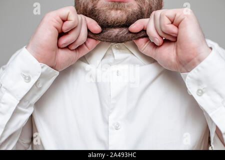 Bärtige Person selbst kneifen auf seinem Doppelkinn, ein weißes Hemd auf grauem Hintergrund Stockfoto