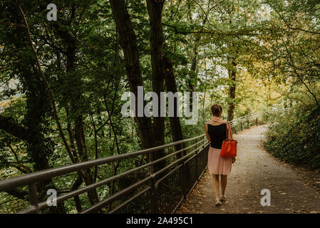 Ein Mädchen in einem Pfad gehen mit Laub auf einer sonnigen Herbst Tag in einem Park, Lifestyle Bild, Film Effekt Stockfoto