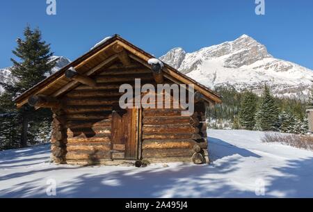 Alte Holzhütte außen und schneebedeckte Rocky Mountain Peak Skyline. Banff National Park, Kanadische Rocky Mountains, Malerische Winterlandschaft Stockfoto